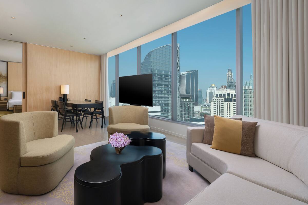 Une chambre d’hôtel moderne avec vue sur la ville, un coin repas et un espace de vie comprenant un canapé et des fauteuils.