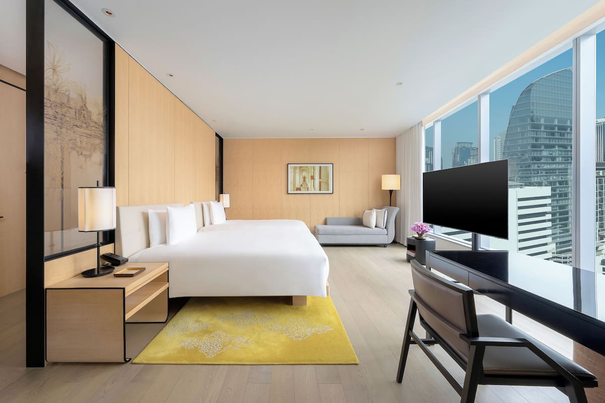 Une chambre d’hôtel moderne dotée d’un grand lit, d’un bureau avec un ordinateur, d’une télévision et offrant une vue sur la ville.