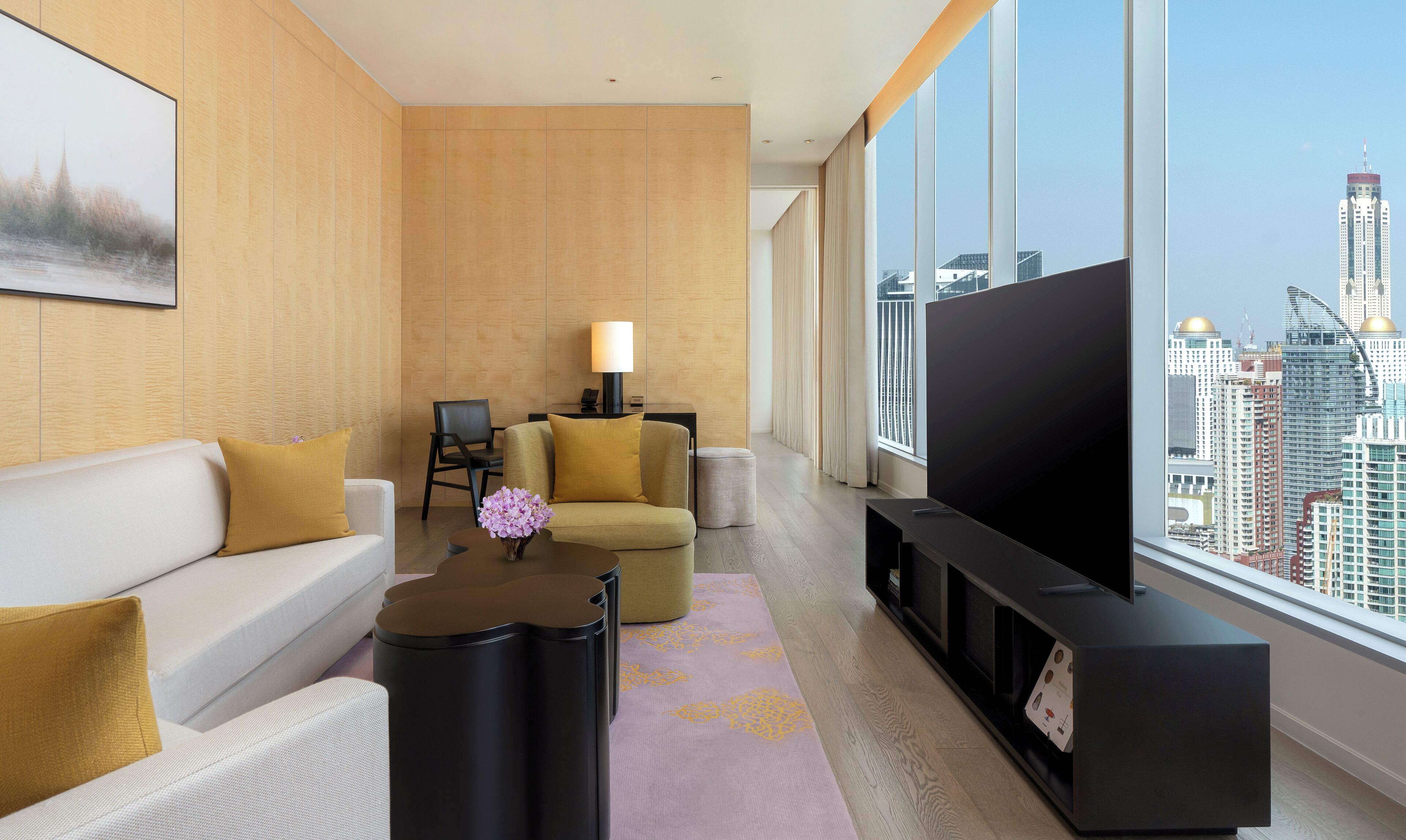 Une chambre d’hôtel moderne dotée d’une grande télévision, d’un canapé, d’un fauteuil, d’une petite table et offrant une vue sur le paysage urbain.