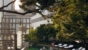 Una piscina con sillones de descanso, rodeada de árboles y edificios modernos.