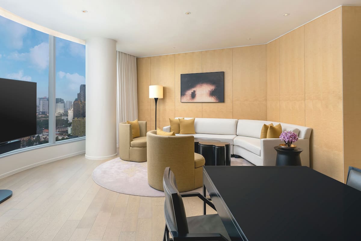 Une chambre d’hôtel moderne dotée d’une grande télévision, d’un canapé, d’une table à manger et offrant une vue sur la ville.