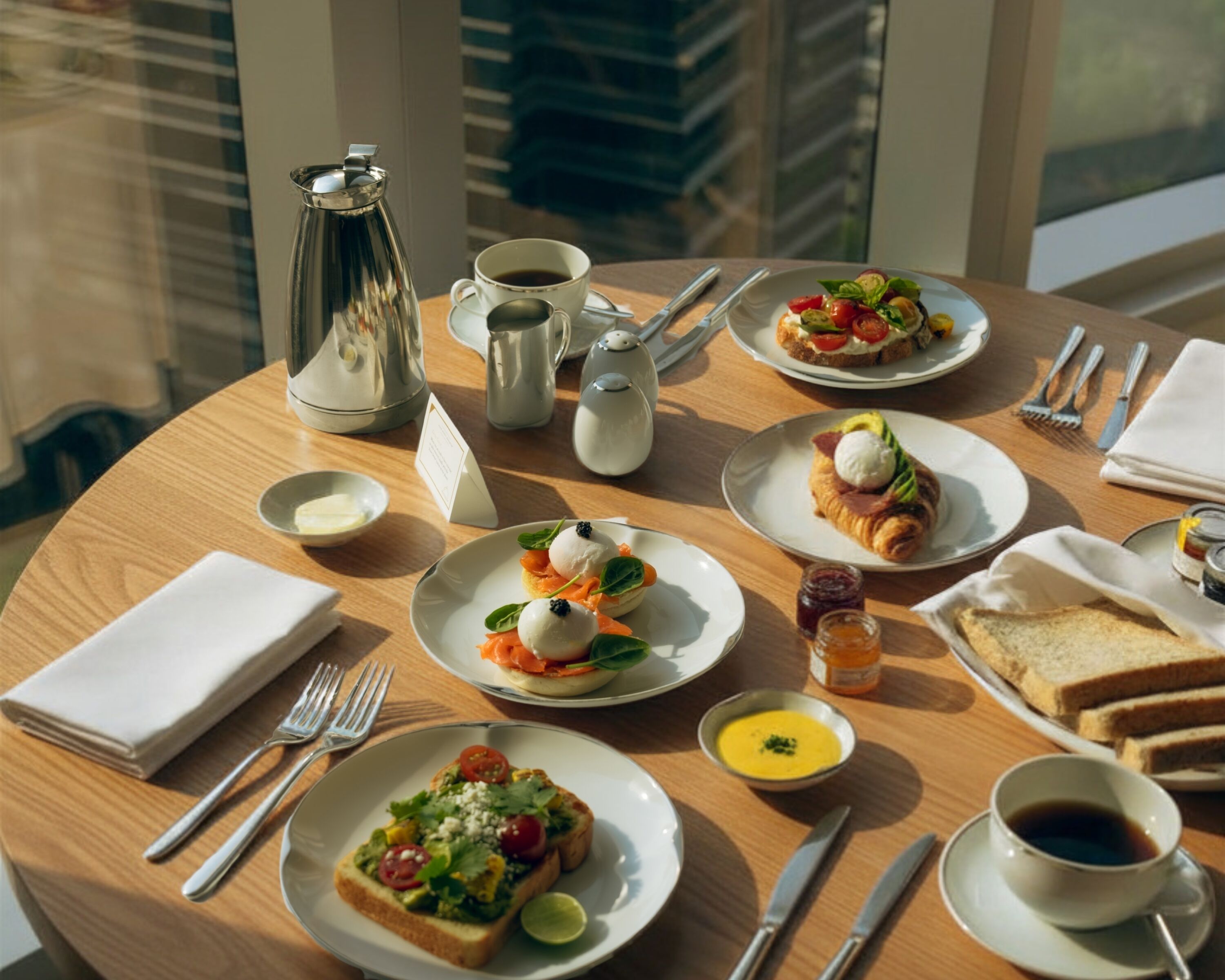 A breakfast setting with plates of food, a coffee pot, and dining utensils on a round table.