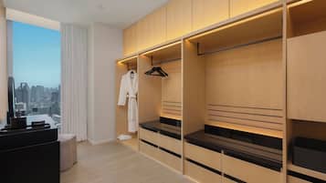 A modern hotel room with a large closet, a vanity with a mirror, and a view of the cityscape.
