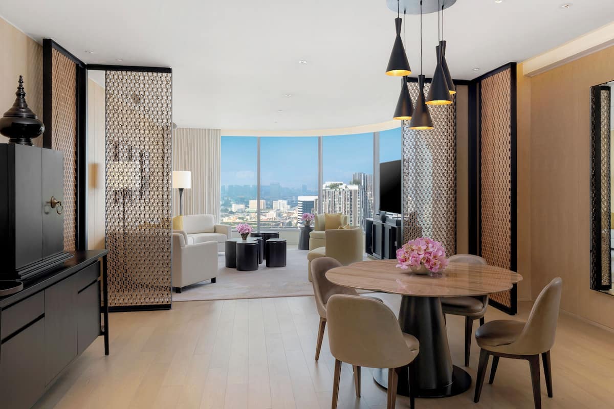 Une chambre d’hôtel moderne offrant une vue imprenable sur la ville, avec un coin repas comprenant une table ronde et des chaises, ainsi qu’un téléviseur fixé au mur.