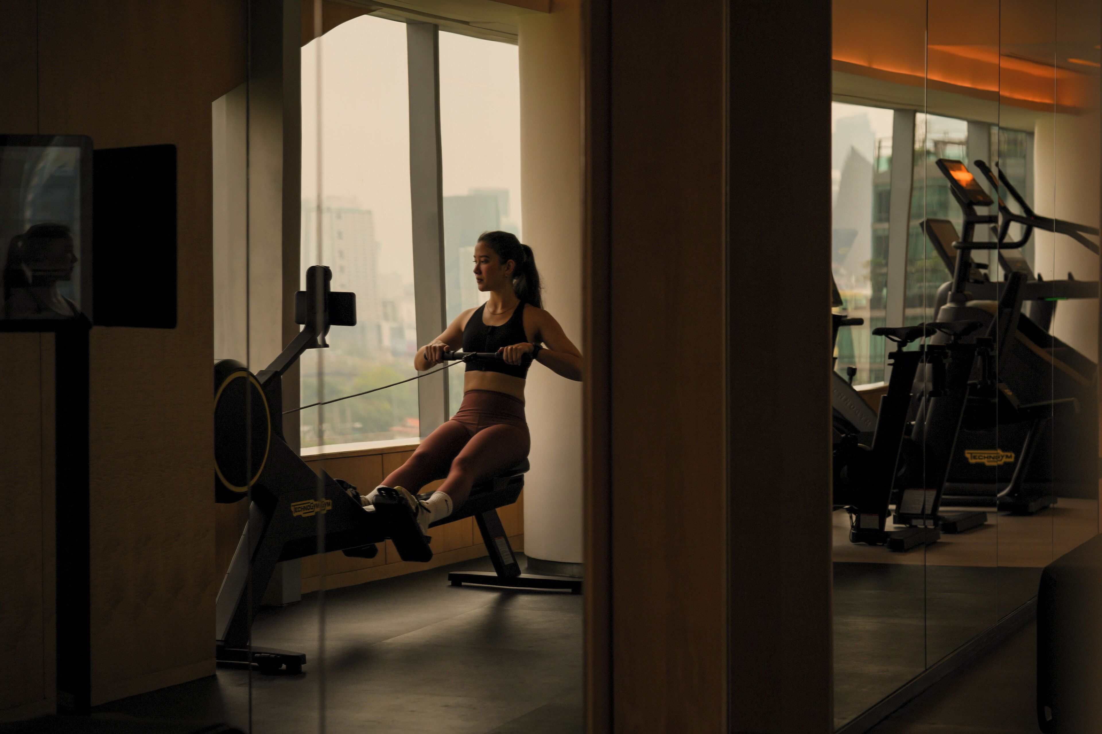 A gym with exercise equipment, large windows, and a city view.