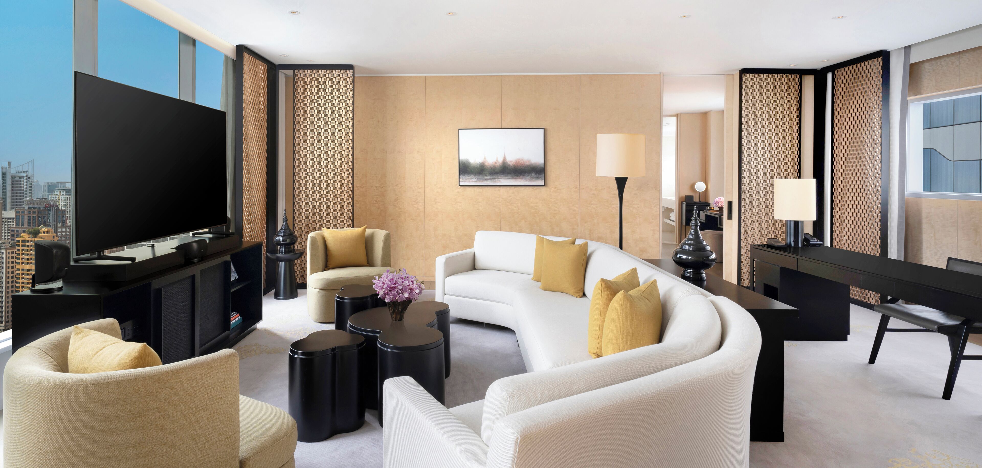 Una habitación de hotel moderna con un televisor de pantalla plana grande, un sofá, dos sillones, una mesa de centro y una mesa de comedor.