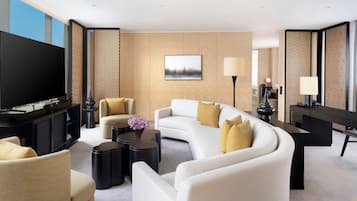 Una habitación de hotel moderna con un televisor de pantalla plana grande, un sofá, dos sillones, una mesa de centro y una mesa de comedor.