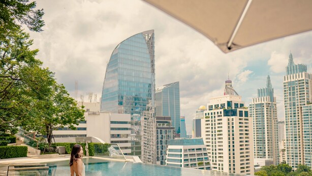 Una mujer está junto a una piscina, con un paisaje urbano al fondo.