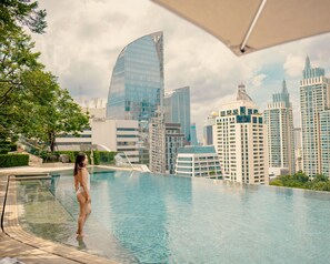 Une femme se tient près d’une piscine, avec une vue sur la ville en arrière-plan.
