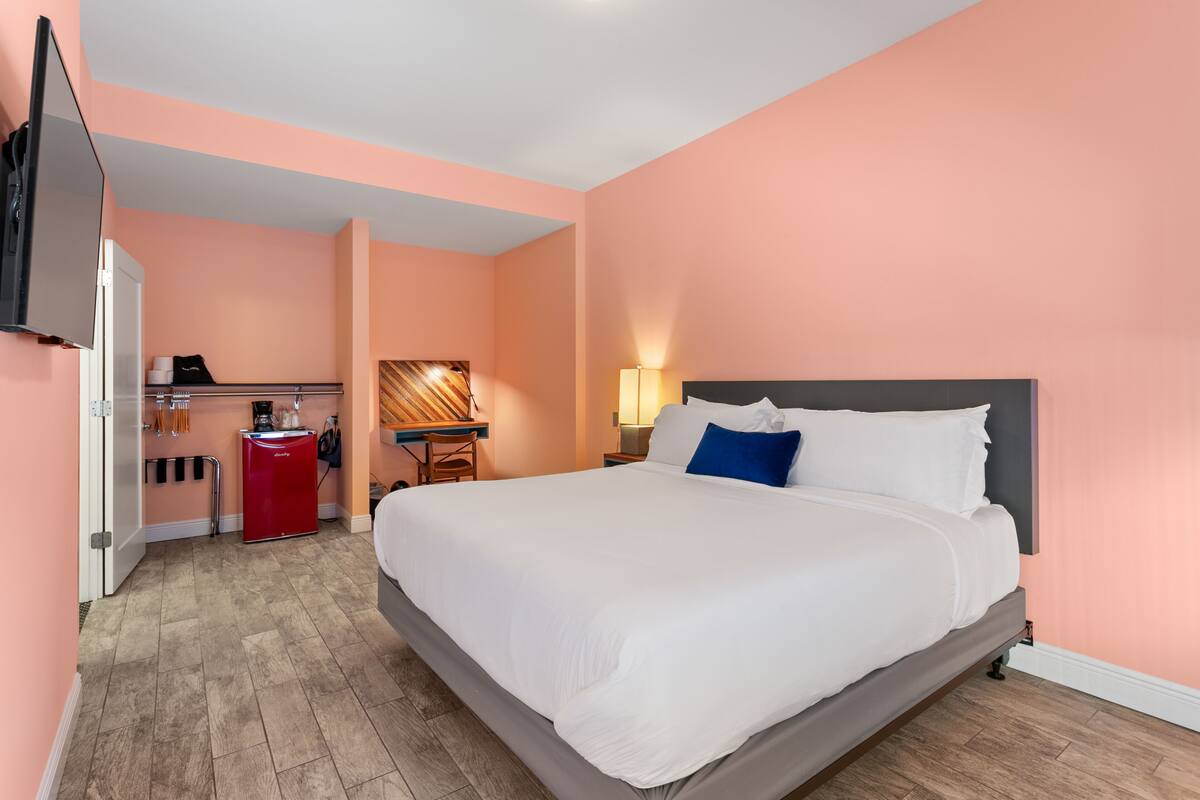 Quarto de hotel com uma cama grande, uma escrivaninha com computador, frigorífico e televisão na parede.