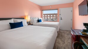 Hotellihuone, jossa on kaksi sänkyä, työpöytä, kahvinkeitin, televisio ja ikkuna, josta avautuu näkymä kaupunkiin.