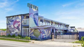 Ein Motel mit einem farbenfrohen Wandgemälde, einem Schild mit der Aufschrift "The Iris Motel" und einem eingezäunten Parkplatz.