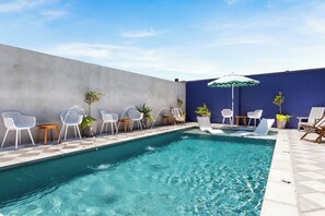 A swimming pool with white chairs and a blue wall. - The Iris Motel (New Orleans)