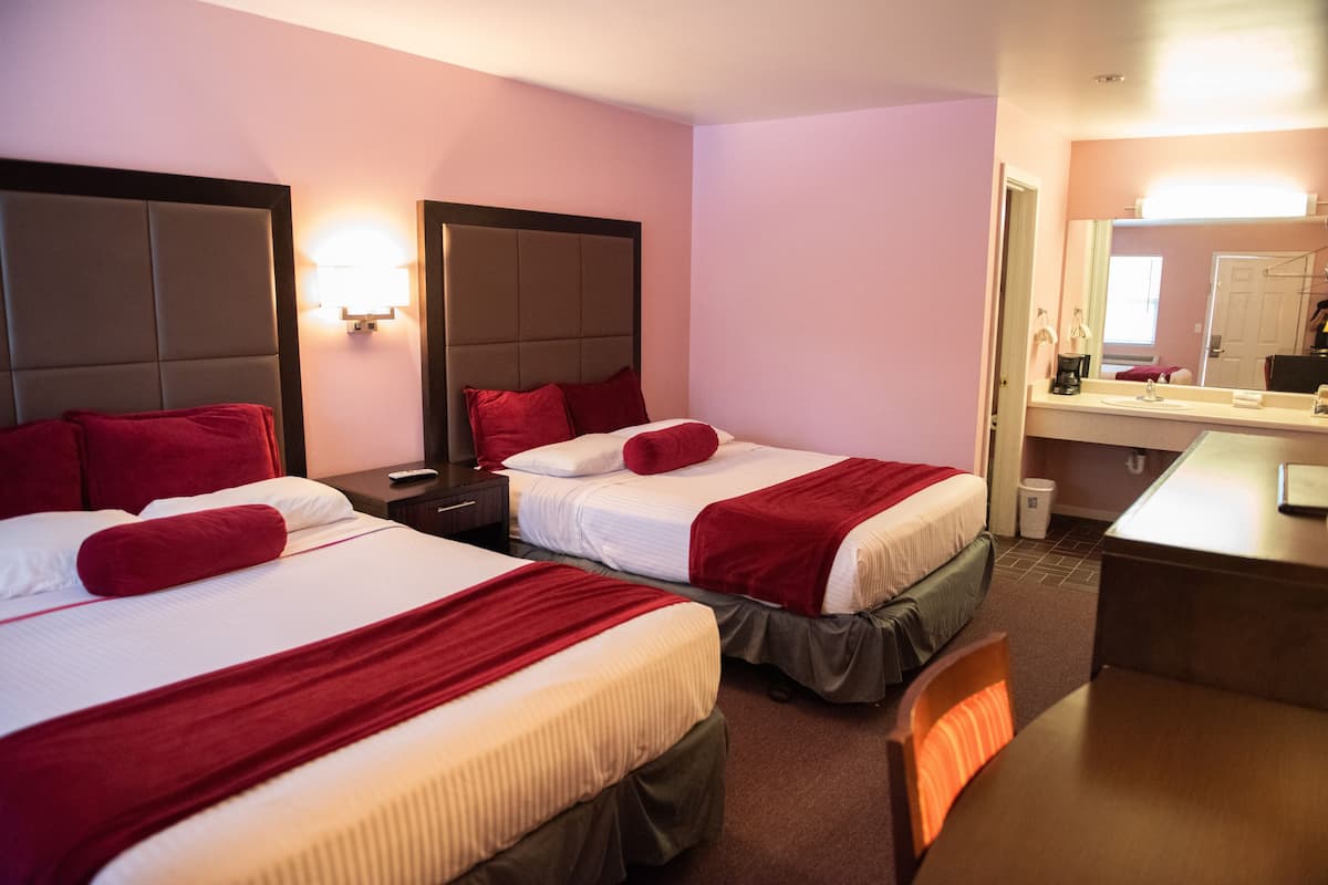 A hotel room with two beds, each with red pillows and headboards, a small desk, and a mirror.