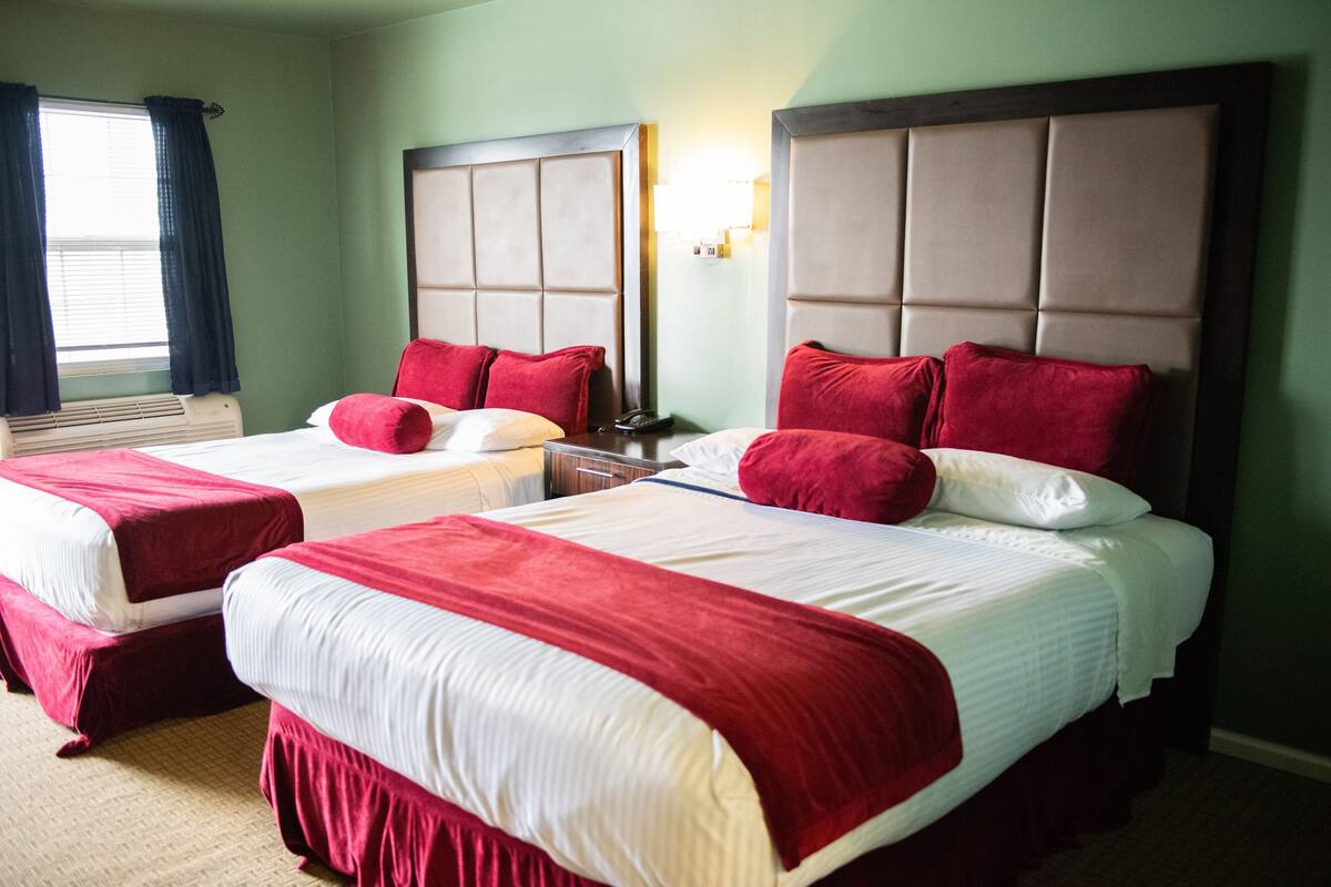 A hotel room with two beds, each with red and white bedding, and a large window with curtains.