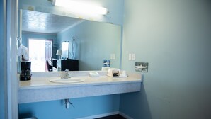 A bathroom with a white sink, a mirror, and a trash can. - Cottonwood Inn (Salem)