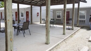 A covered outdoor seating area with tables and chairs, wooden posts, and a gravel path leading to a building with red doors. - Cottonwood Inn (Salem)