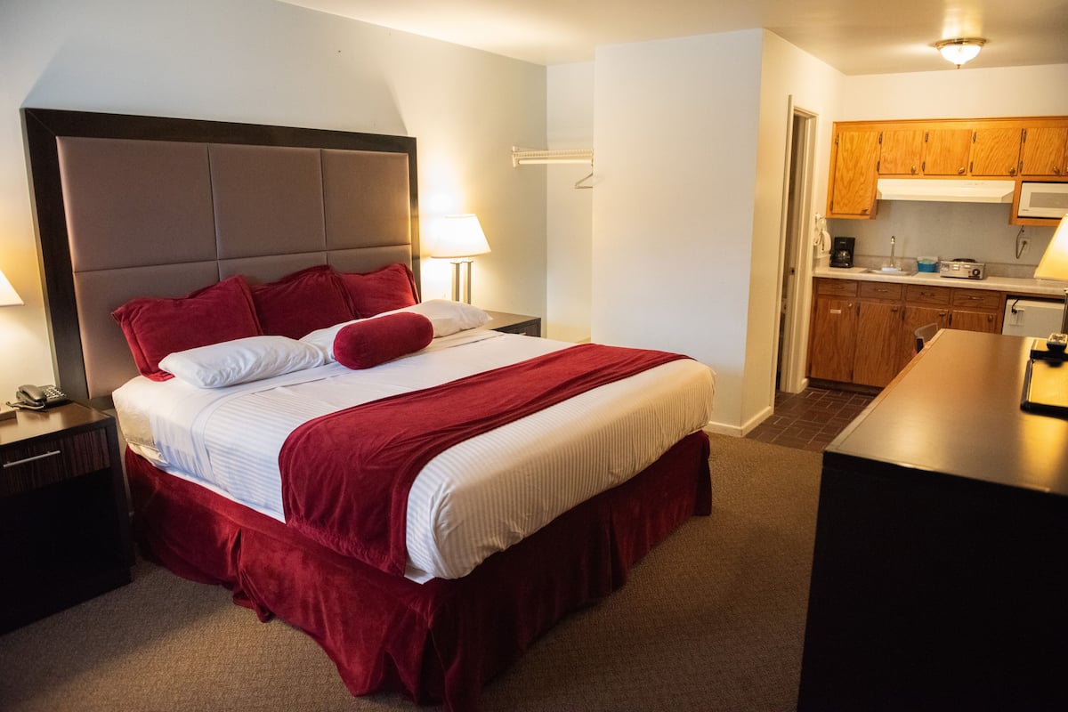 A hotel room with a large bed, a nightstand, a desk, and a kitchenette.