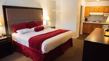 Una habitación de hotel con una cama grande, una mesita de noche, un escritorio y una kitchenette.
