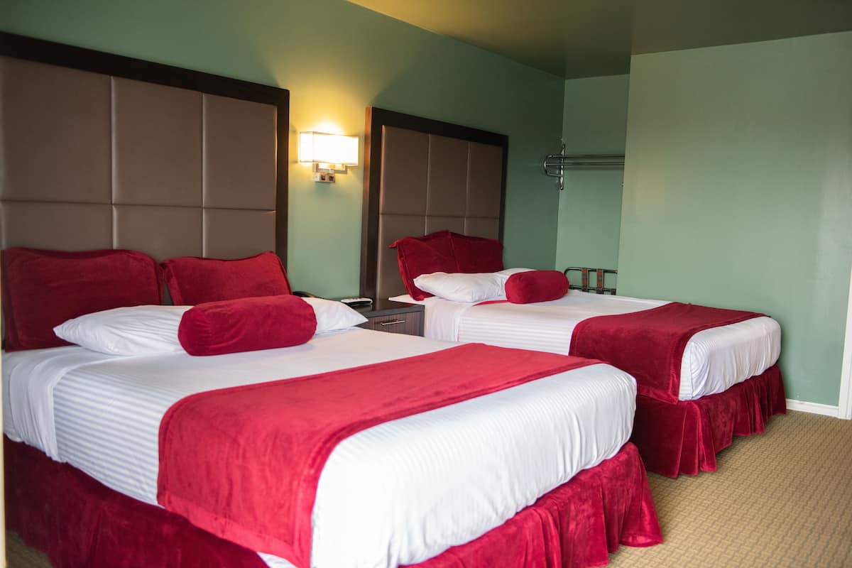 A hotel room with two beds, each with red bedding and white pillows, a nightstand, a lamp, and a mirror.