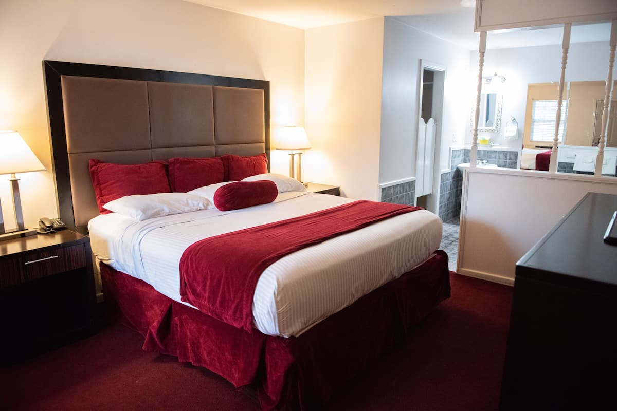 A hotel room with a large bed, two bedside tables, a nightstand, a dresser, and a mirror.