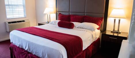 A neatly made bed with red and white bedding, two bedside lamps, and a window with blinds.
