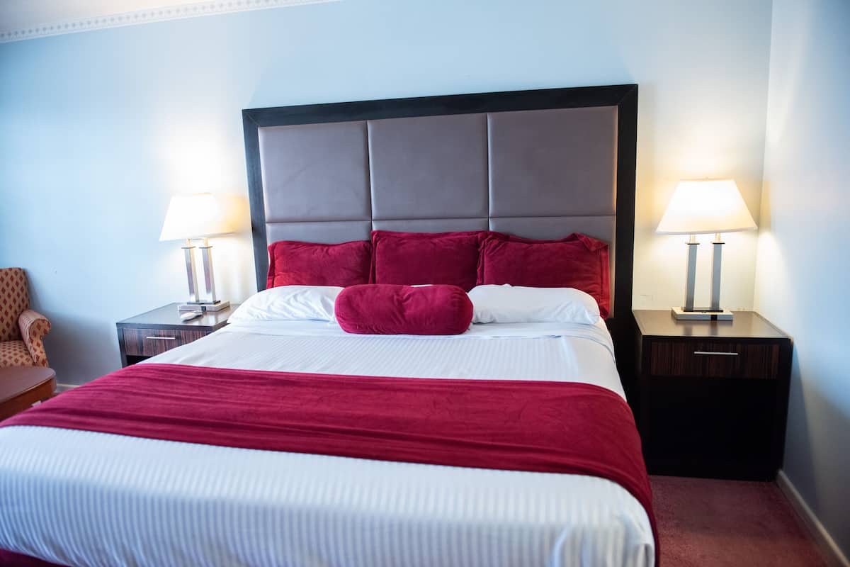 A hotel room with a large bed, two bedside tables with lamps, a red throw blanket, and a red pillow.