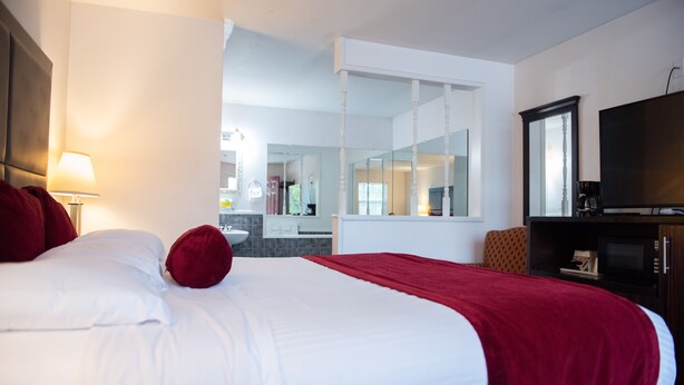 A hotel room with a large bed, a TV, a mirror, and a view of the bathroom. - Cottonwood Inn (Salem)