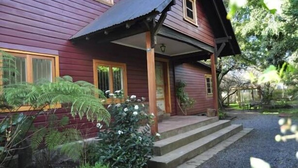 Uma casa de madeira com varanda, degraus e entrada por um caminho de cascalho.