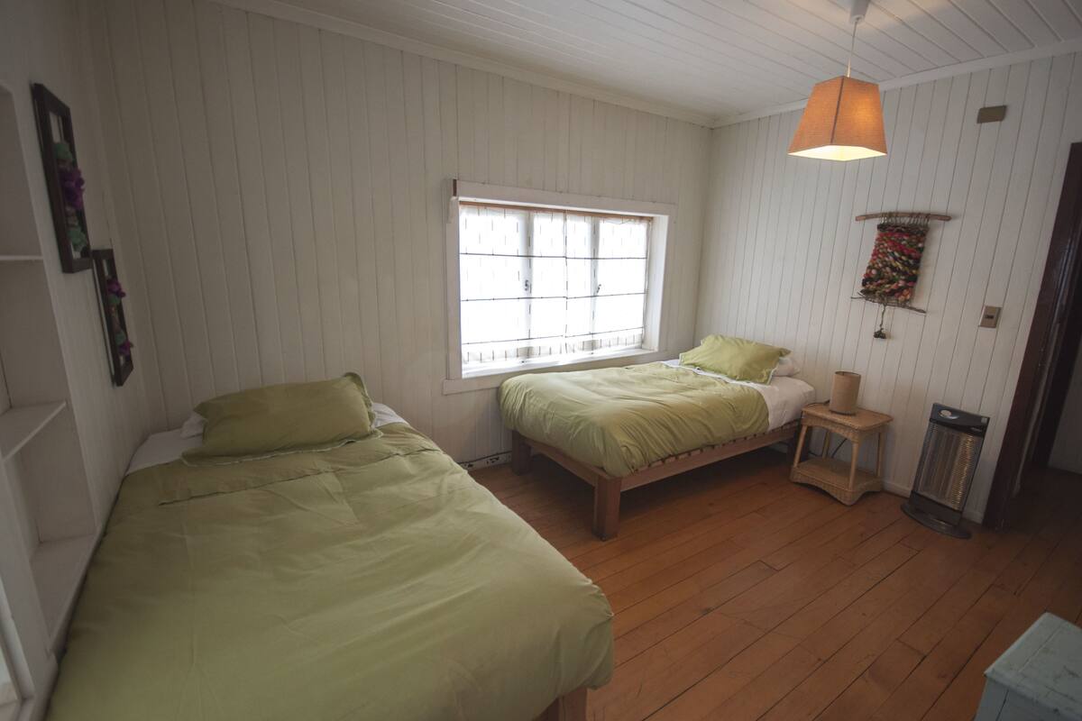 Ein Zimmer mit zwei Einzelbetten, einem Fenster, einer Heizung und einer Pendelleuchte.