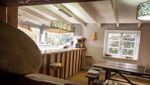 Interior rústico com mobiliário de madeira, espaço de bar e janela com vista para vegetação.