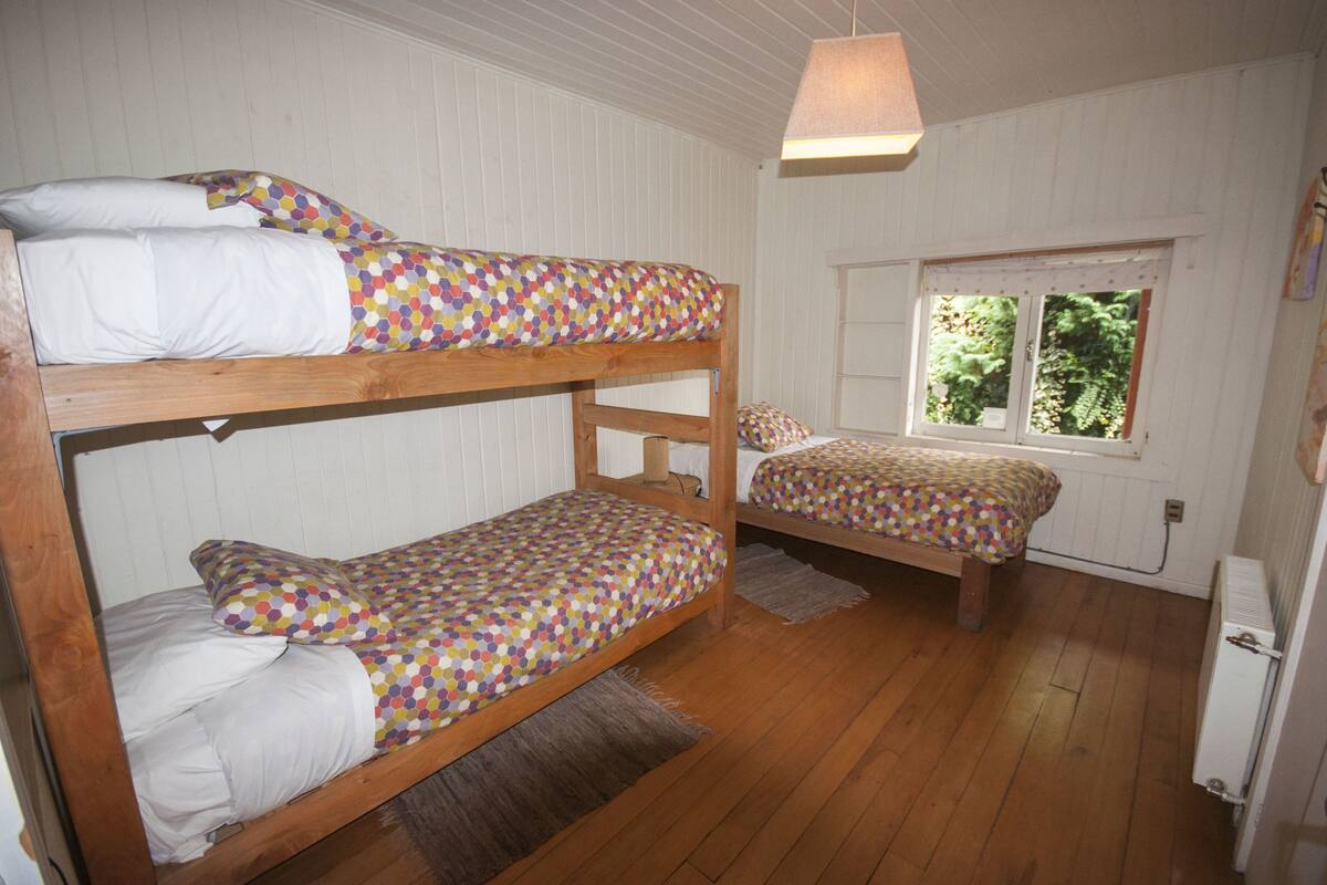 Ein Zimmer mit zwei Etagenbetten, Holzboden, einem Fenster mit Blick auf Grünflächen und einer hängenden Leuchte.