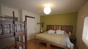 Quarto com cama de madeira, um banco, porta branca e parede verde.