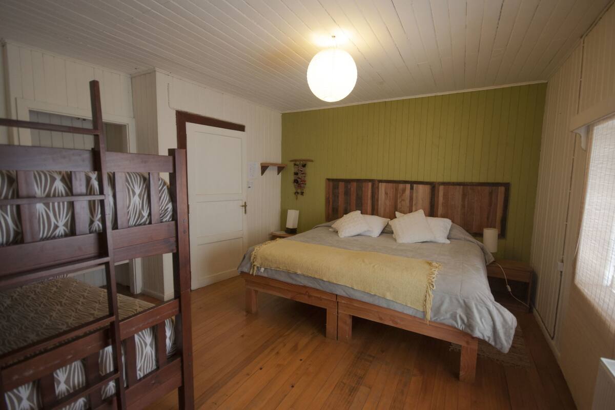 Ein Schlafzimmer mit einem hölzernen Bett, einer Bank, einer weißen Tür und einer grünen Wand.