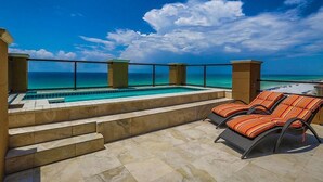 A rooftop pool area with a clear view of the ocean, steps leading to the pool, and two lounge chairs.