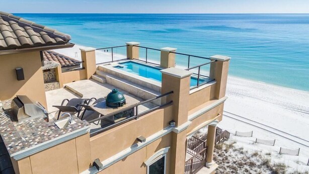 A beachfront property with a rooftop pool, outdoor seating, and a view of the ocean.