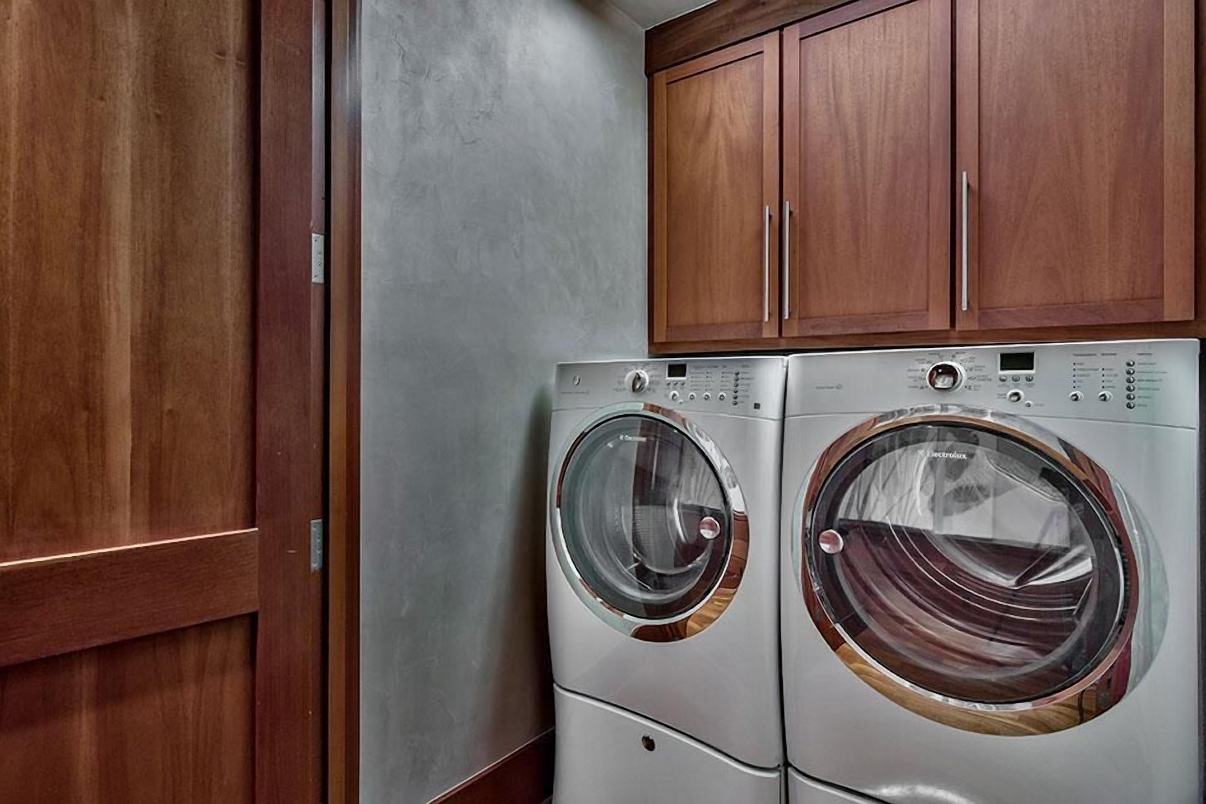 A compact laundry room with two front-loading washing machines and wooden cabinets above.