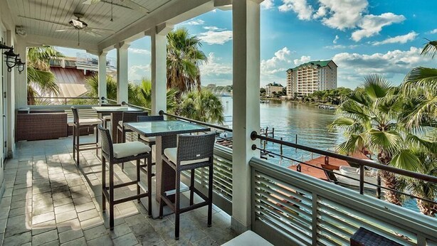 A covered outdoor area with a table and chairs, overlooking a body of water and a building in the distance. - OLYMPIA CORAL SUITE 3 Bedroom Holiday Home by Five Star Properties (Destin)
