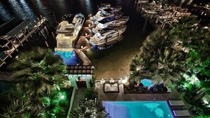 A pool area with multiple boats docked, surrounded by palm trees and lounge chairs. - OLYMPIA CORAL SUITE 3 Bedroom Holiday Home by Five Star Properties (Destin)