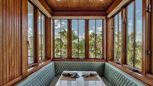 A room with a long bench, large windows, and a view of palm trees. - OLYMPIA CORAL SUITE 3 Bedroom Holiday Home by Five Star Properties (Destin)