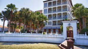 A multi-story hotel with balconies, palm trees, and a waterfront view.