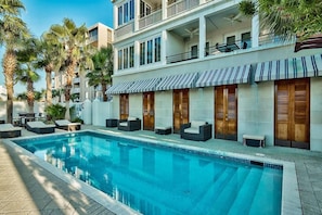 Un hotel moderno con piscina, mobiliario exterior y un edificio de varios pisos con balcones.