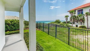 Un balcon avec vue sur la mer, un bâtiment blanc avec un toit rouge et une pelouse bien entretenue.