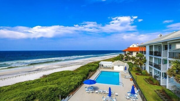 Un hôtel situé en bord de mer, doté d’une piscine, de chaises longues et offrant une vue sur l’océan.