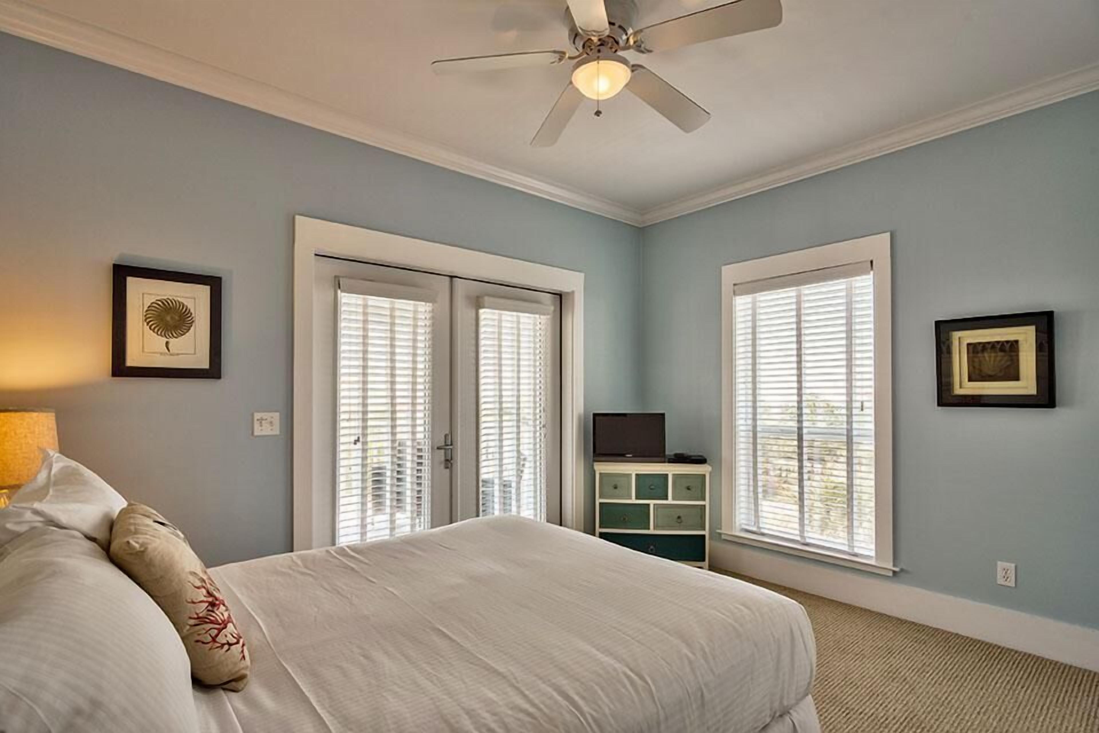 A bedroom with a bed, a ceiling fan, a TV on a stand, and two doors with windows.