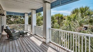 Une terrasse en bois, dotée de mobilier d’extérieur, de rampes blanches et offrant une vue sur les palmiers.