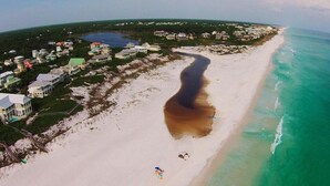 Vue aérienne d’une zone côtière avec une plage, des maisons et une rivière.