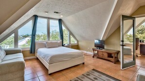 Quarto com teto inclinado, uma cama, uma televisão e vista para o exterior.
