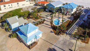 Ett flygbildsfoto av ett semesterområde med flera byggnader, en pool och en strand.