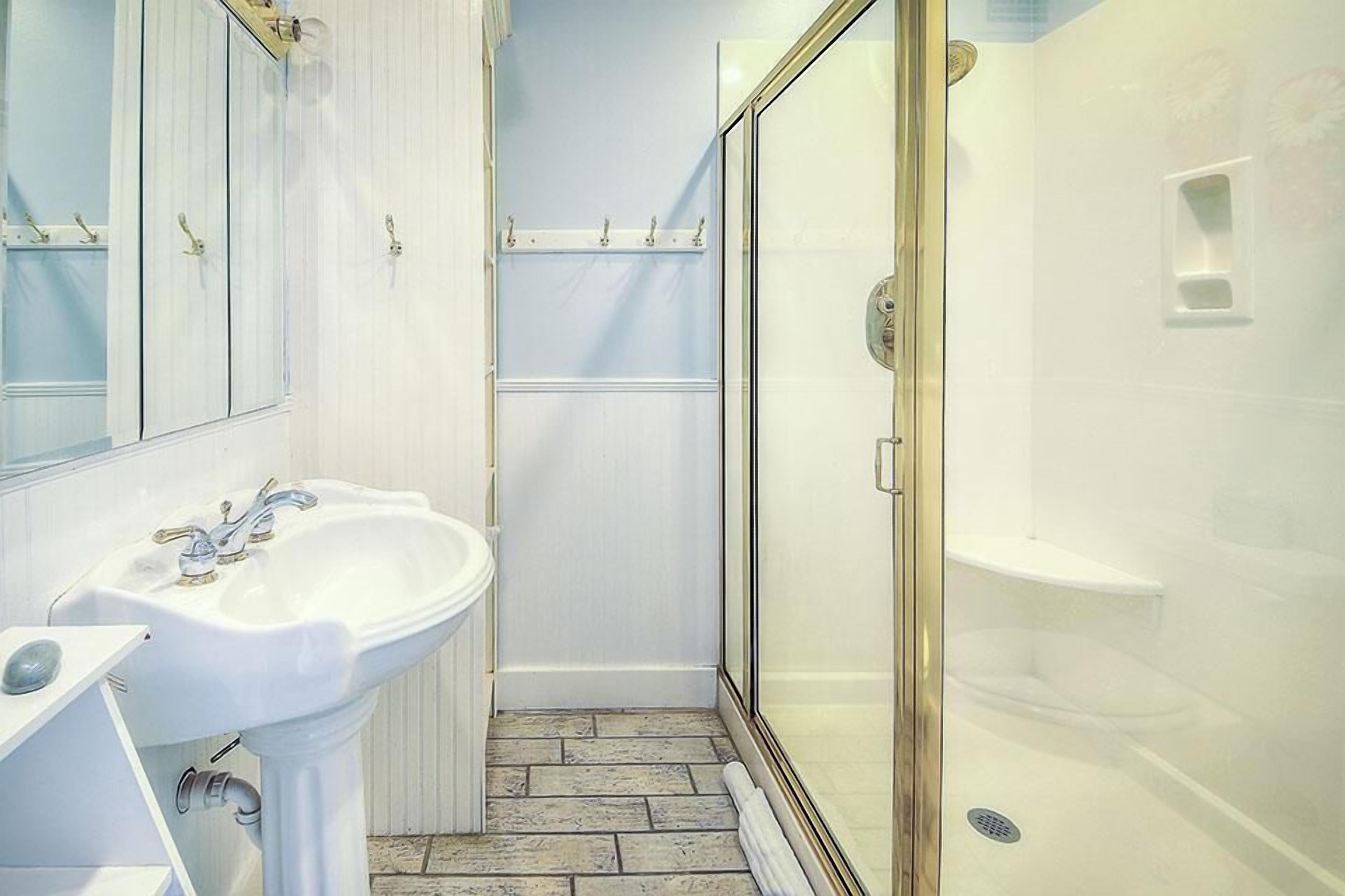 A bathroom with a white sink, a glass shower enclosure, and a tiled floor.